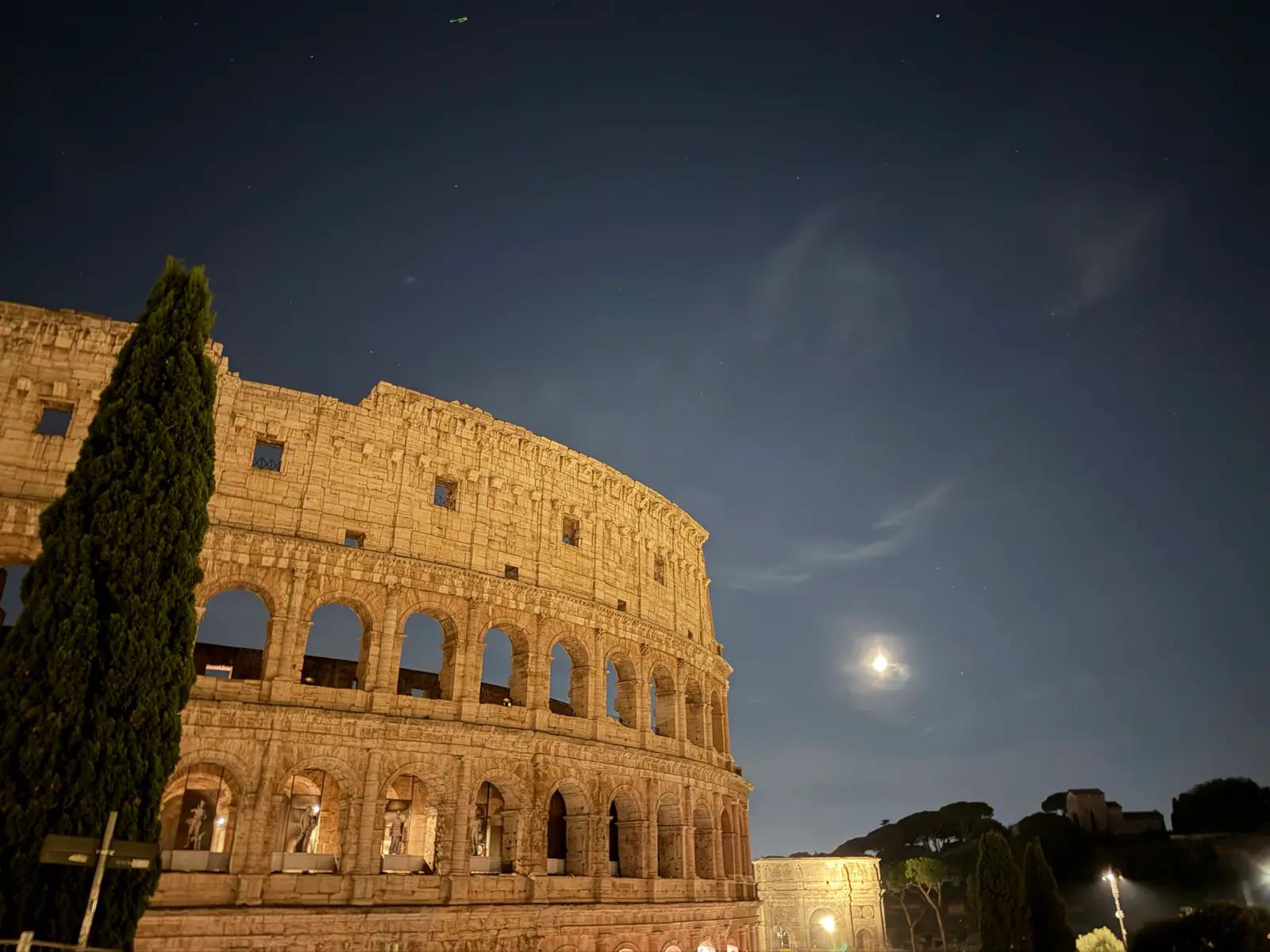 Illuminated Colosseum at night with the moon in the sky.