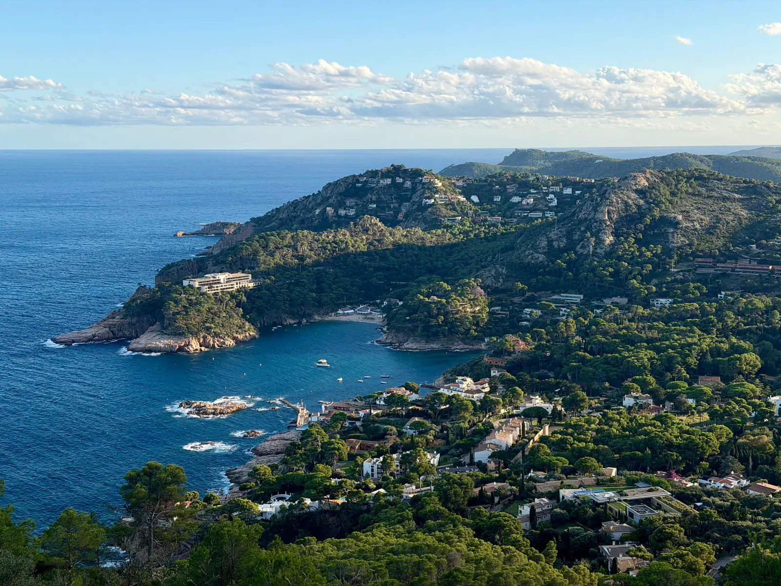 A coastal bay with green hills, rocky shoreline, and houses scattered across the landscape.