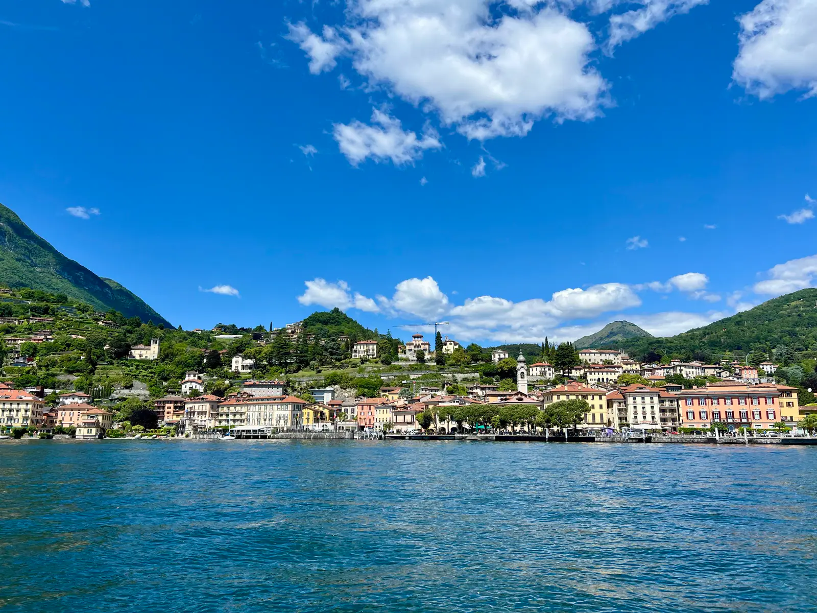 A lakeside town with colorful buildings, green hills, and a blue sky with clouds.